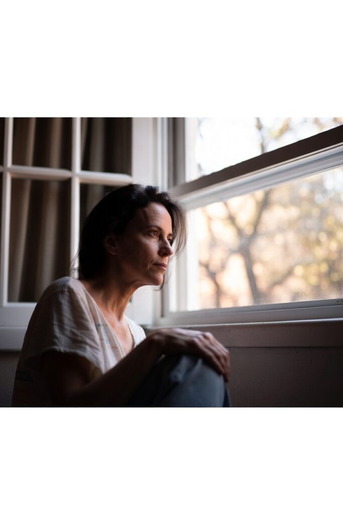 Mulher sentada à janela em momento de reflexão profunda representando os sinais de que a alma está pedindo uma mudança