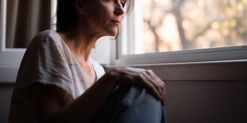 Mulher sentada à janela em momento de reflexão profunda representando os sinais de que a alma está pedindo uma mudança