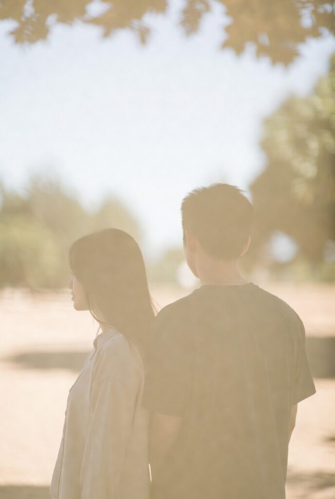 Duas pessoas de costas com ombros próximos mas sem se tocar, luz suave — presença e distância ao mesmo tempo