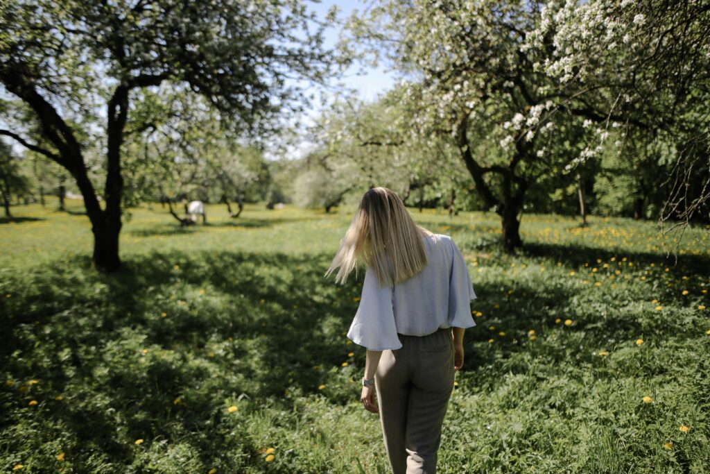Pessoa caminhando sozinha por trilha na natureza com luz da manhã filtrando pelas árvores, postura relaxada, sem celular