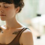 Pessoa sentada em posição relaxada com olhos fechados em prática de meditação, luz natural suave e tons neutros