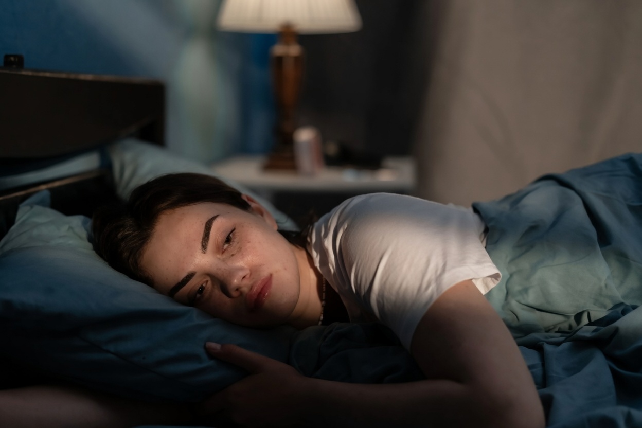 Mulher deitada de olhos abertos olhando o teto, expressão de mente ativa, luz suave e tons neutros