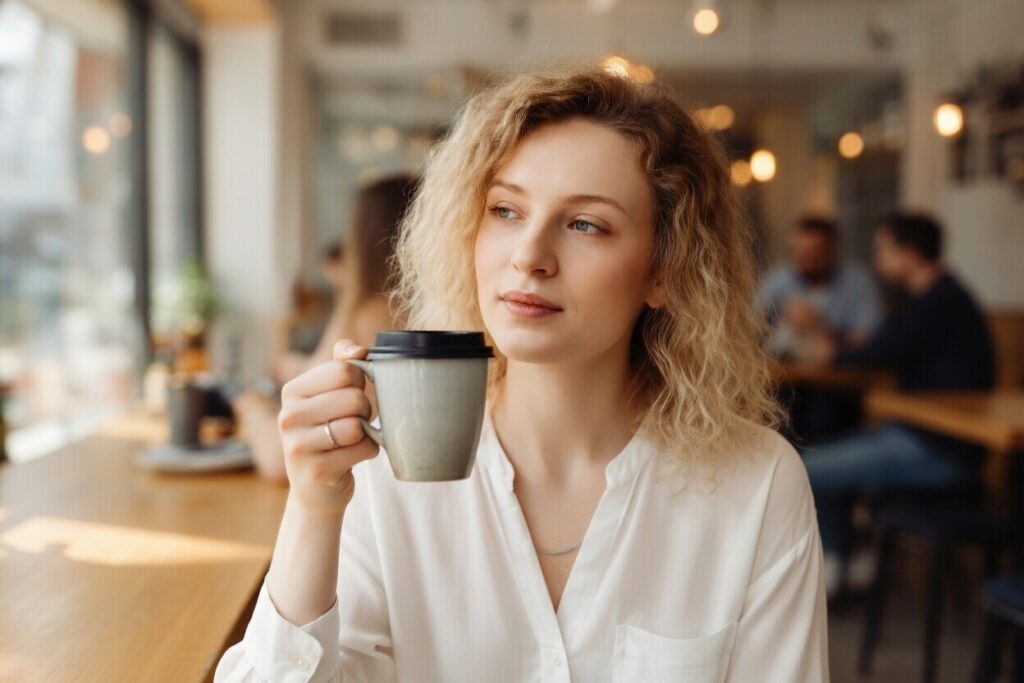 Mulher com expressão levemente ausente em ambiente cotidiano, fisicamente presente mas mentalmente distante, pessoa que pensa demais 